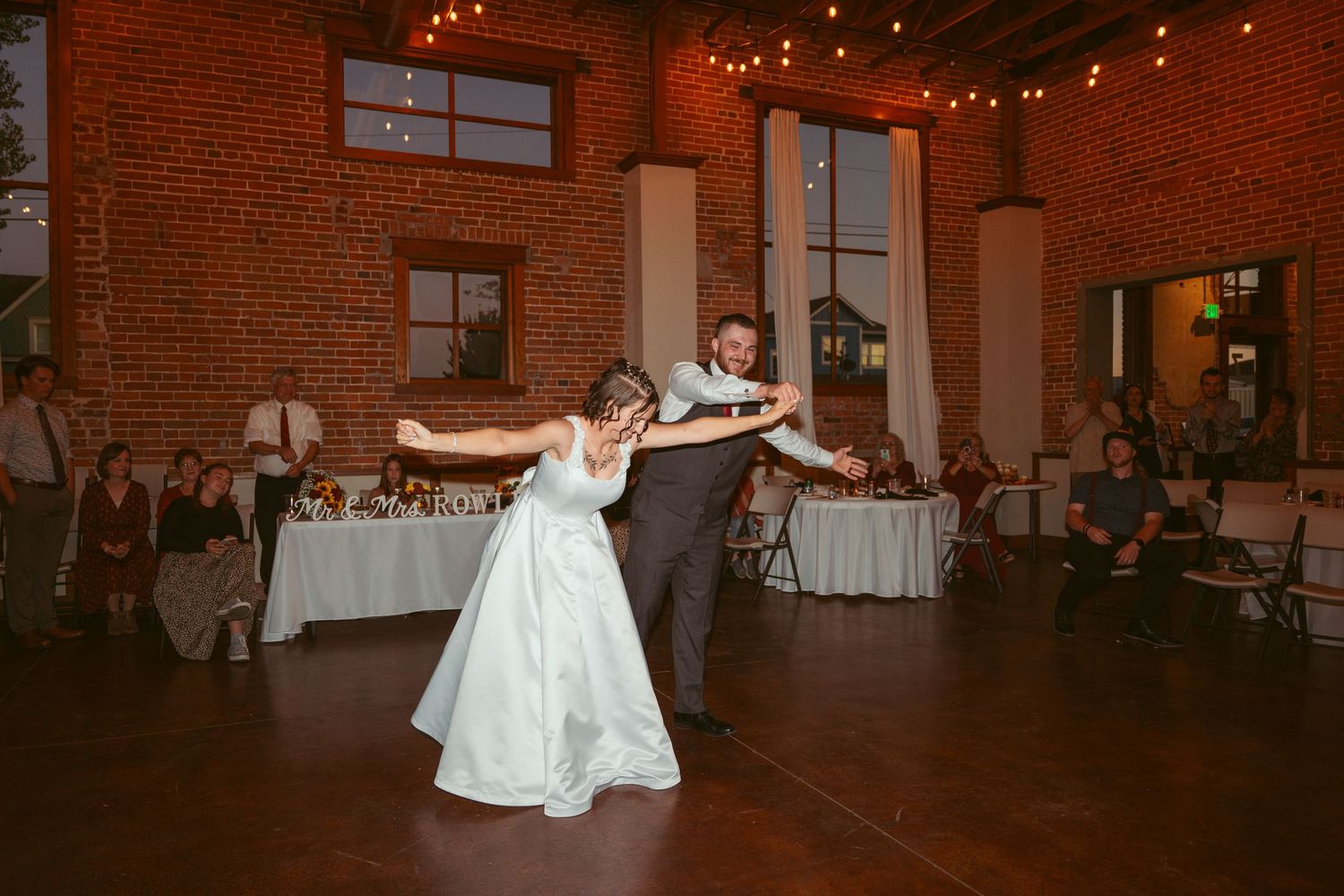 A flowing white dress spins during an elegant dance move in a brick-walled reception space.