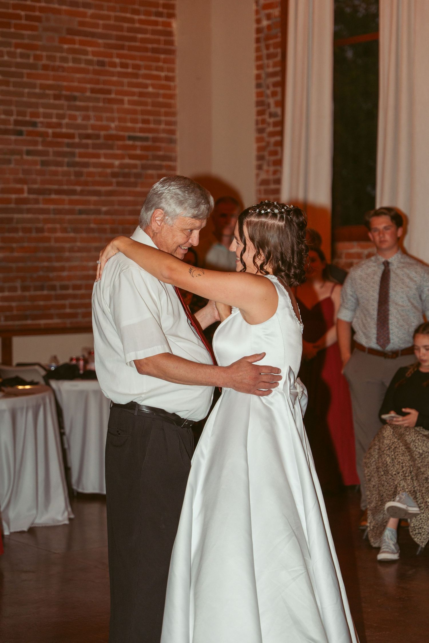 A tender dance embrace at a wedding reception in a rustic brick-walled venue.