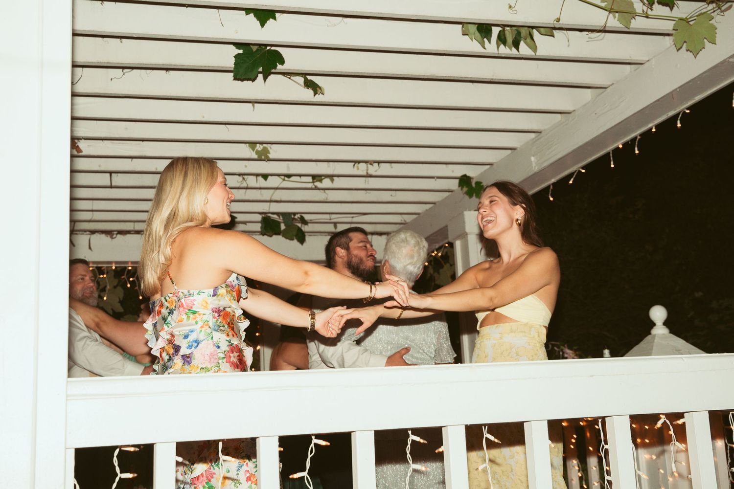 Wedding guests dancing and celebrating together on an outdoor covered patio with string lights.