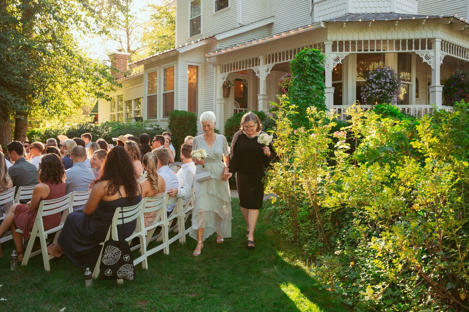 Outdoor wedding venue with white Victorian house and garden setting at golden hour.