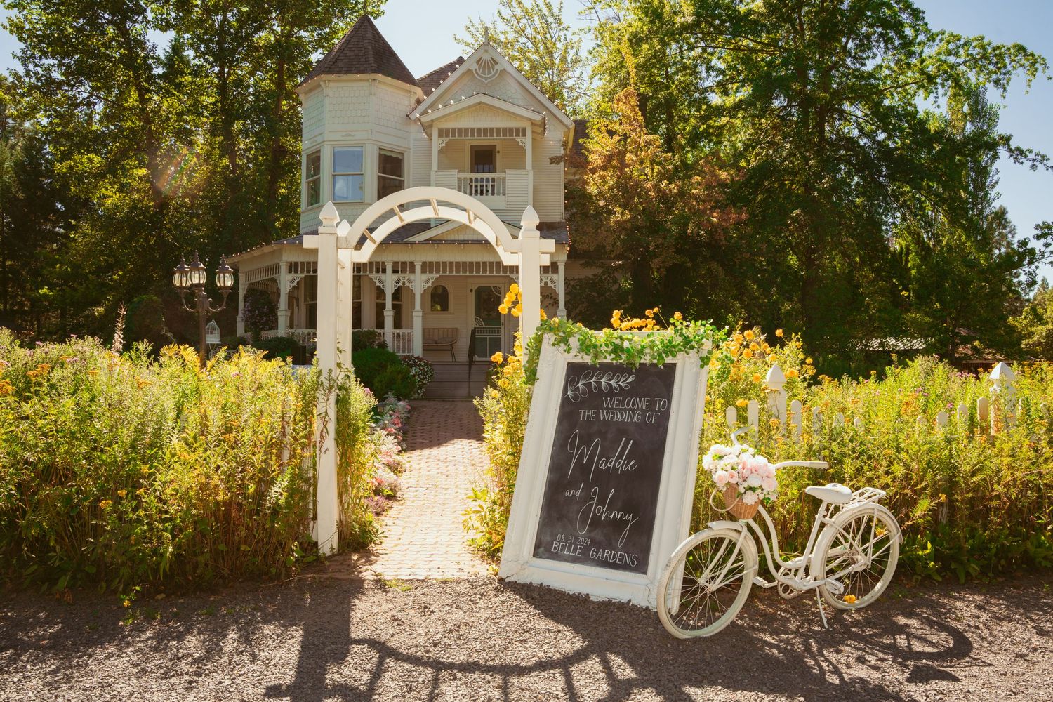 A rustic garden wedding venue with white decorative signs and vintage bicycles along a gravel pathway.