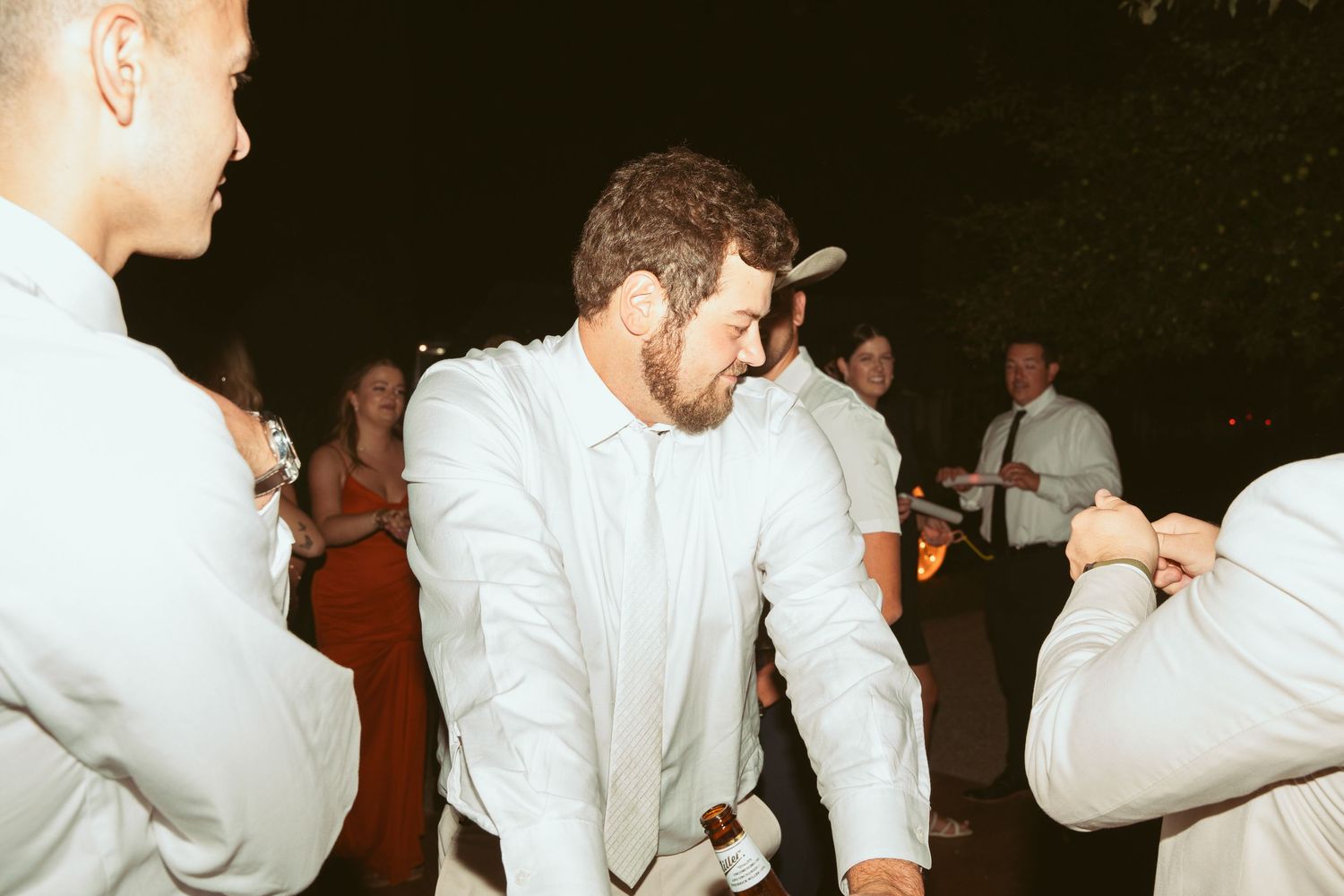 Guests in white attire dancing together at an evening celebration.