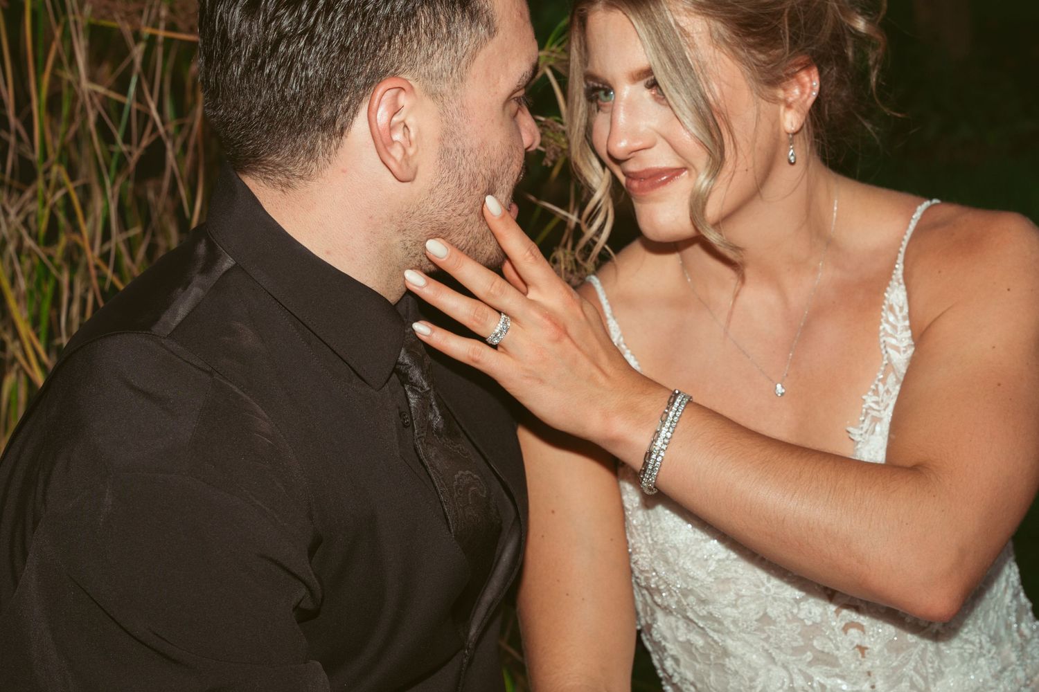 A couple in wedding attire share a romantic kiss in an outdoor evening setting.
