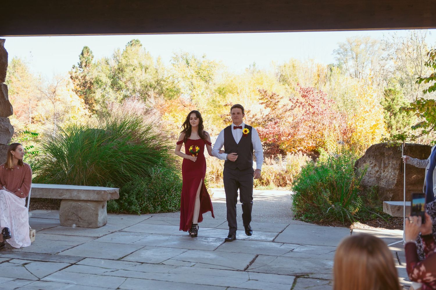 Wedding guests and party members mingle on an outdoor stone patio during a celebration.