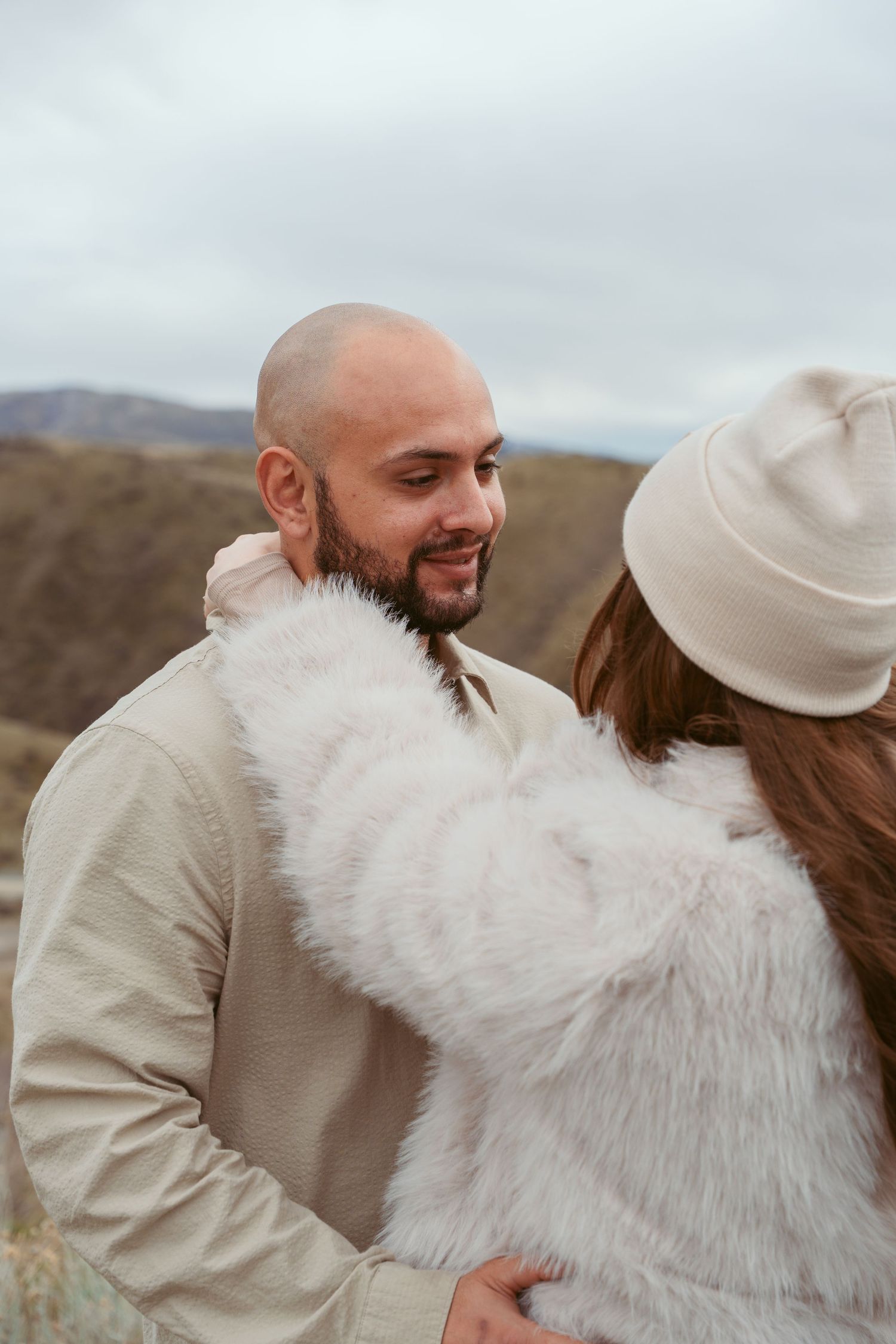 A couple shares an intimate moment outdoors wearing neutral colored clothing.