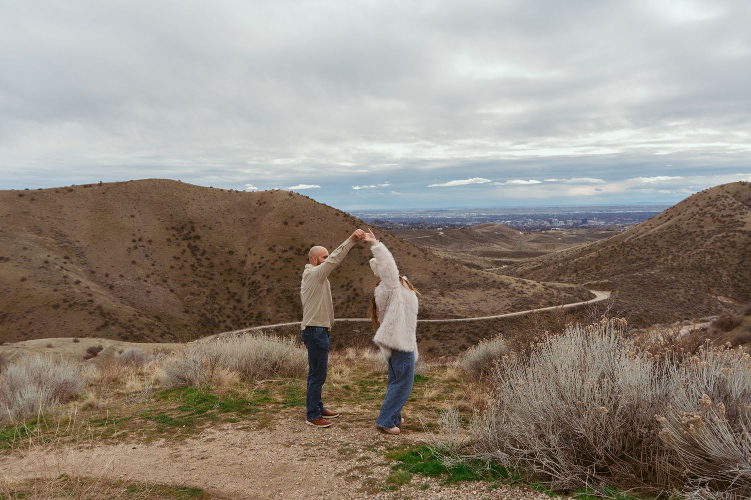A couple holds hands while enjoying a scenic mountain view on a hiking trail.