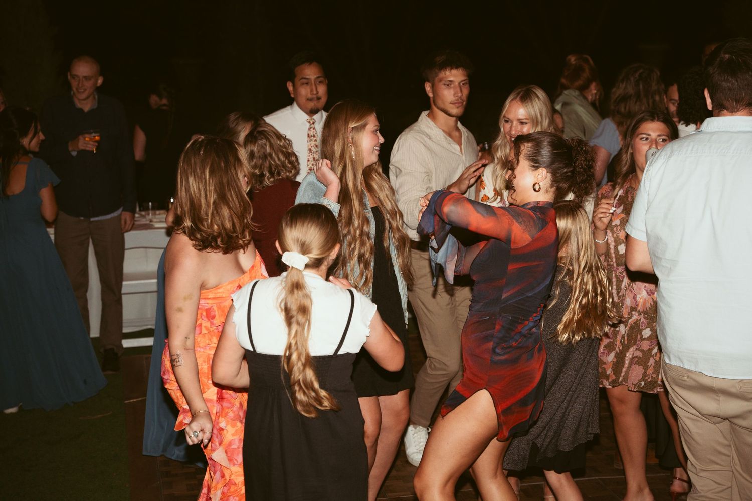 Guests dancing and celebrating at a dimly lit outdoor wedding reception with string lights.