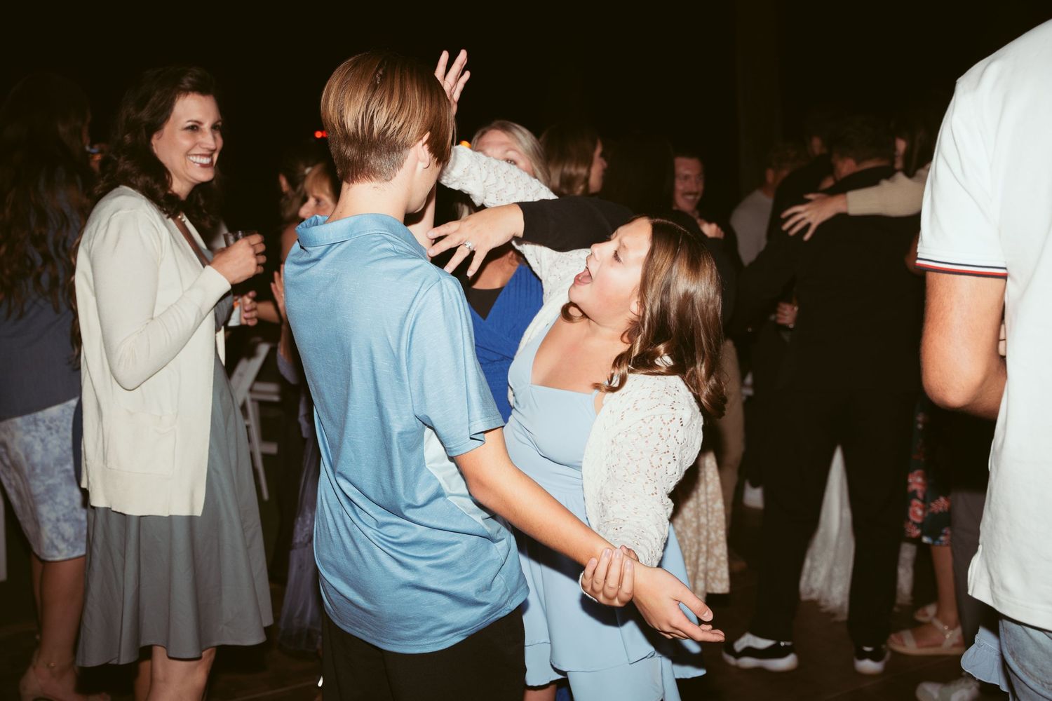 Wedding guests dancing and embracing during an evening outdoor reception.