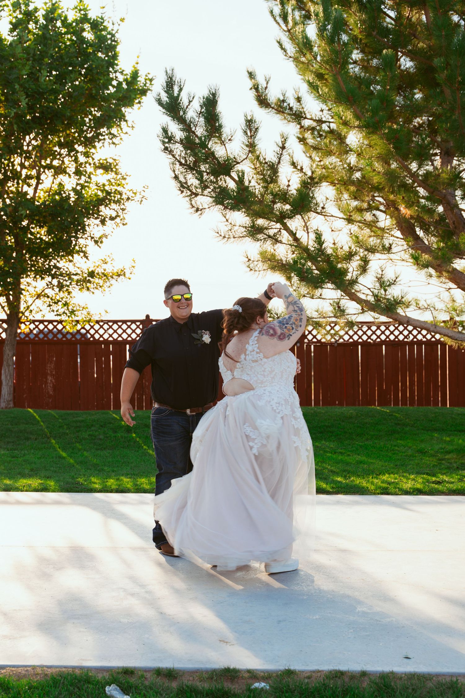 Couple dancing on an outdoor patio with a wooden fence in the background during sunset.