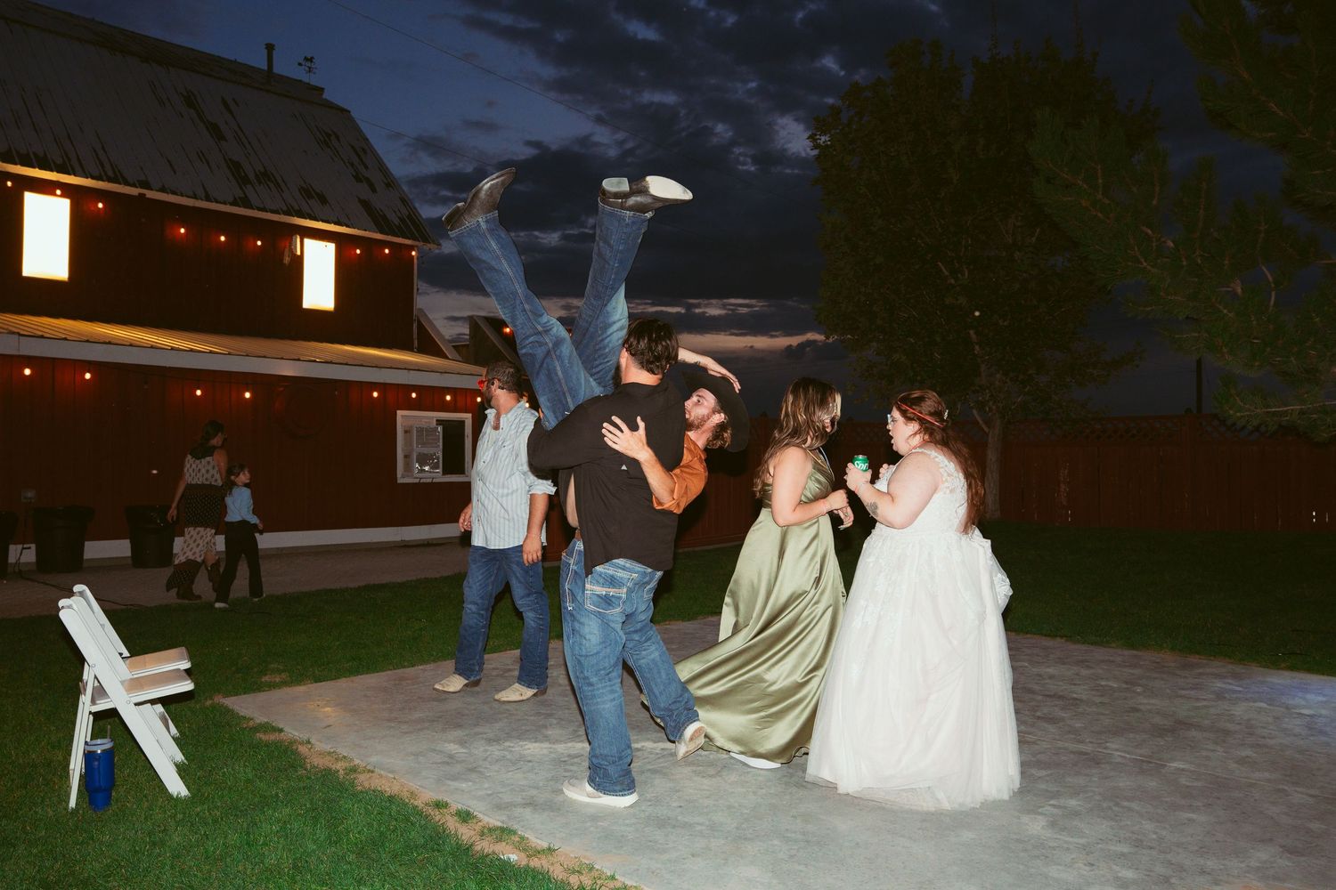 Wedding party dancing and celebrating outdoors at night with string lights overhead.