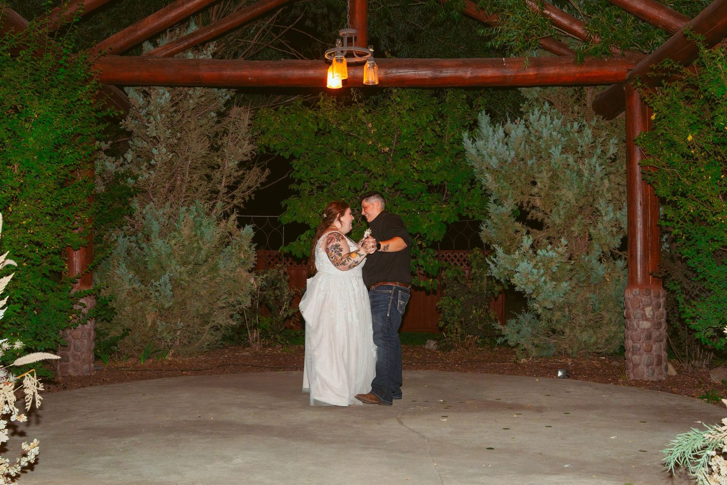 Outdoor wedding venue with wooden pergola and decorative lighting at sunset.