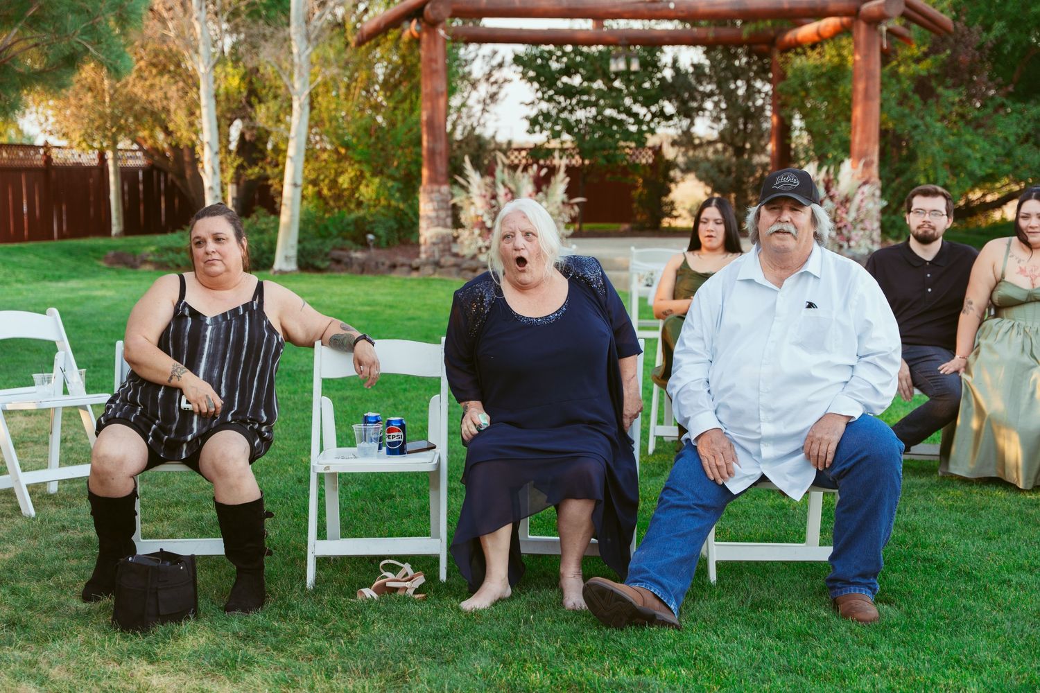 Wedding guests seated on white chairs in an outdoor garden setting.