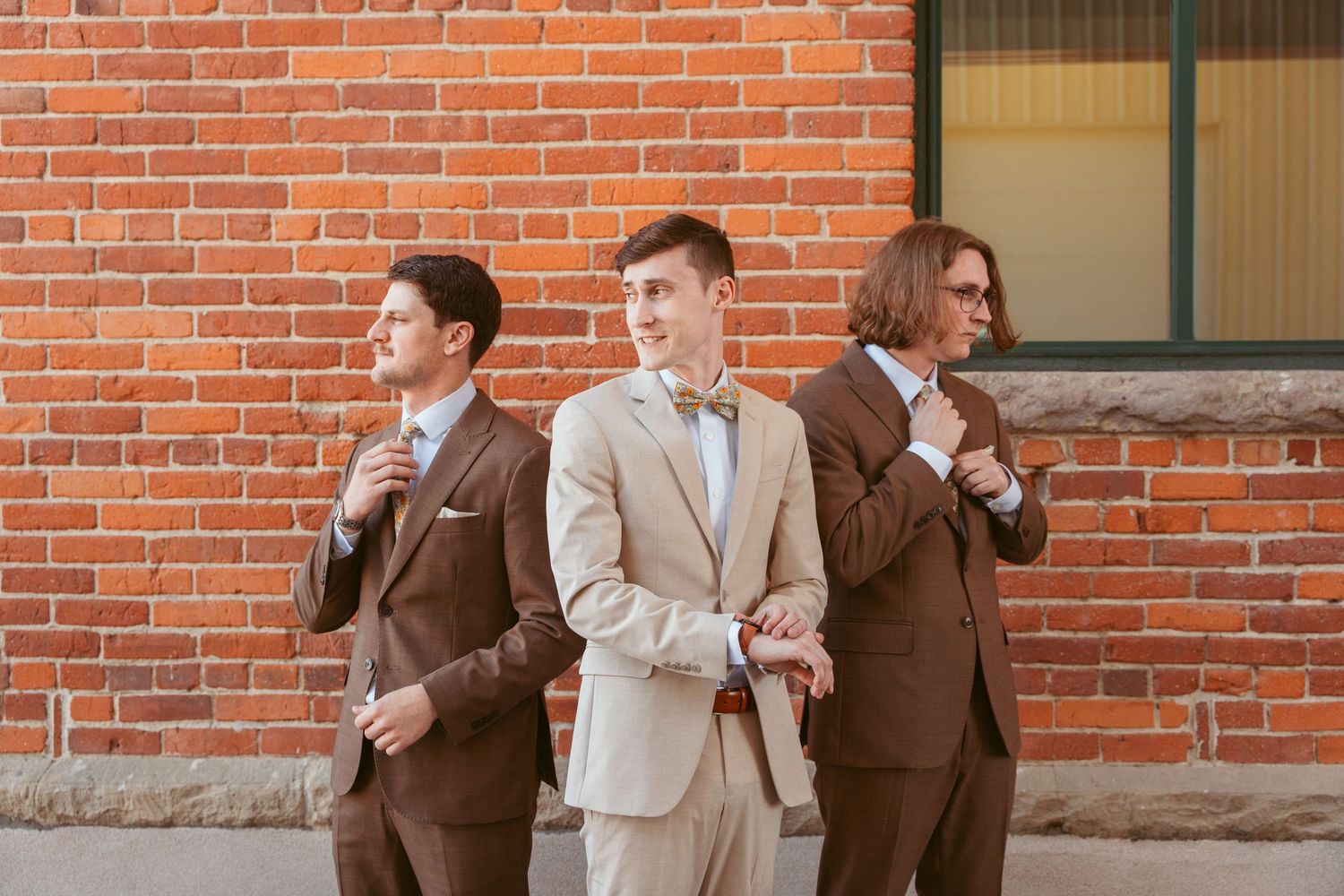 Wedding party members posing against red brick wall of historic building.