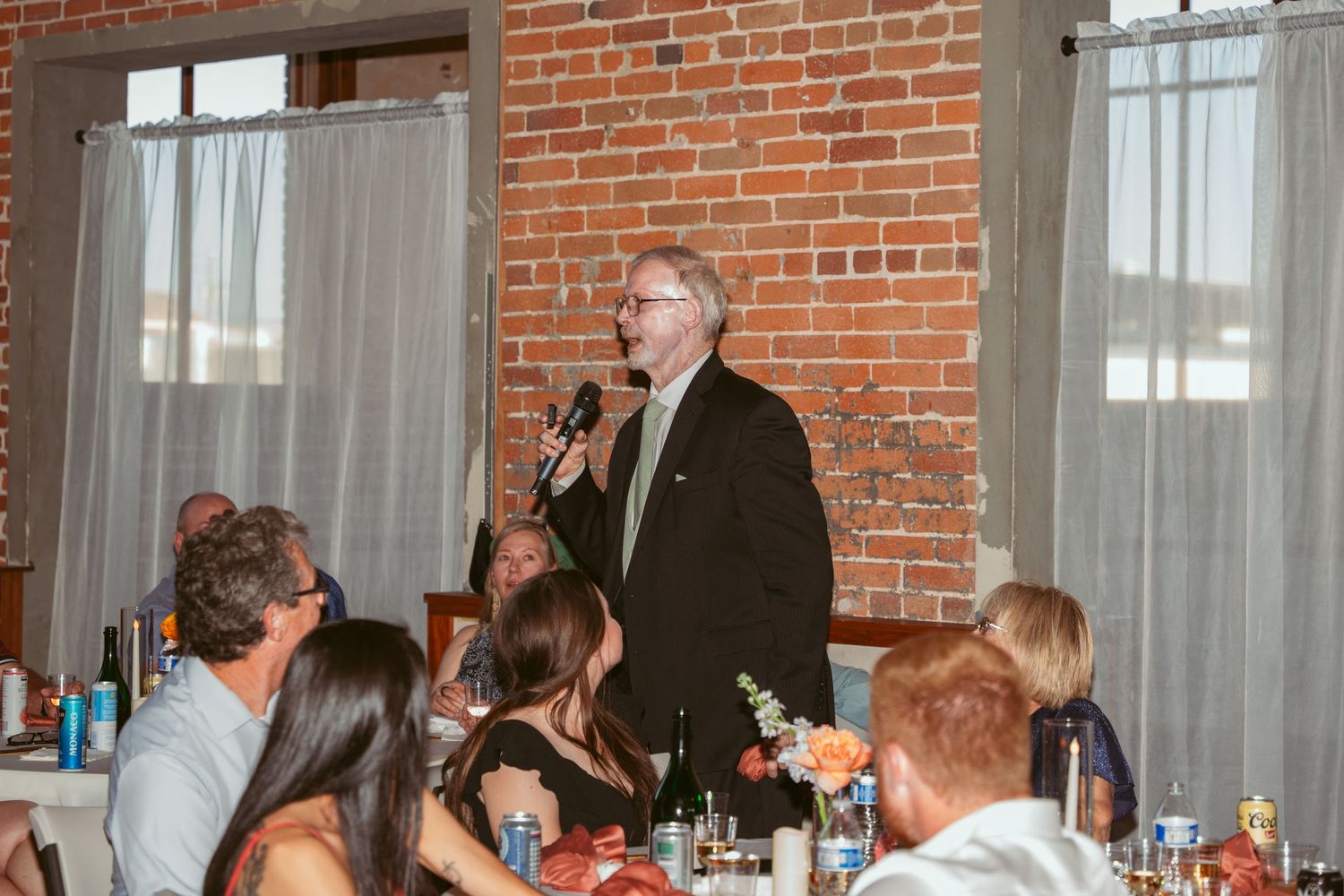 Wedding guests seated at tables in a brick-walled reception venue.