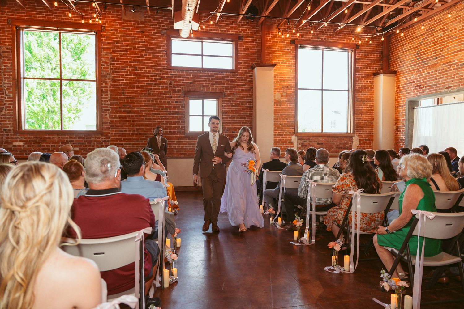 Wedding venue with string lights and large windows illuminating the exposed brick interior.