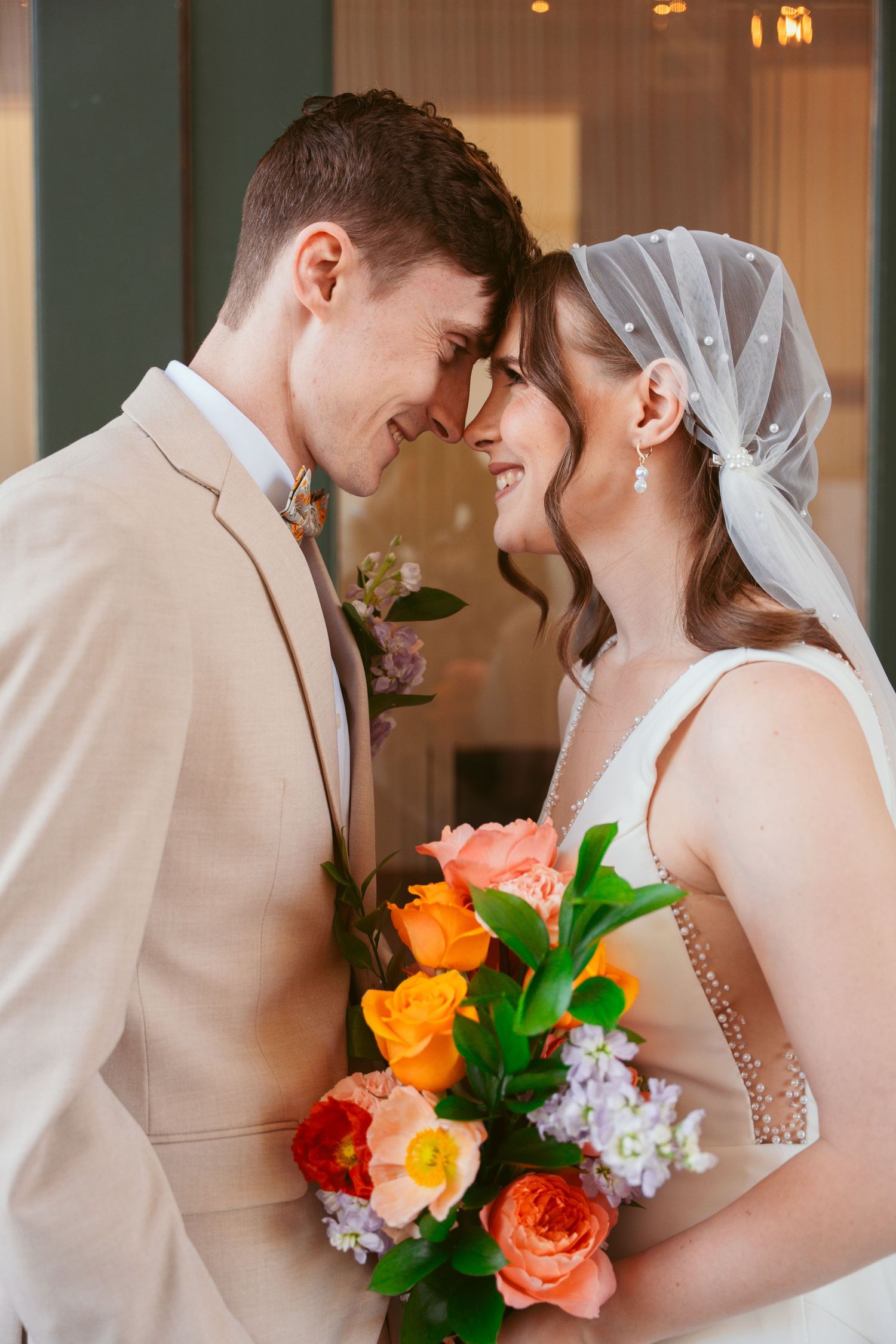 Romantic wedding couple sharing an intimate moment with vibrant orange and coral bouquet.