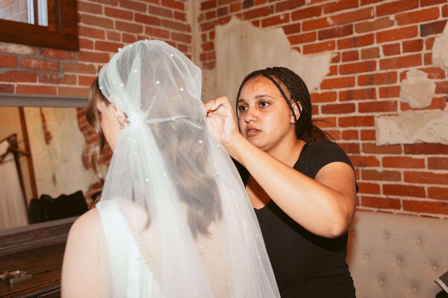 A makeup artist applies finishing touches in a rustic brick-walled venue.