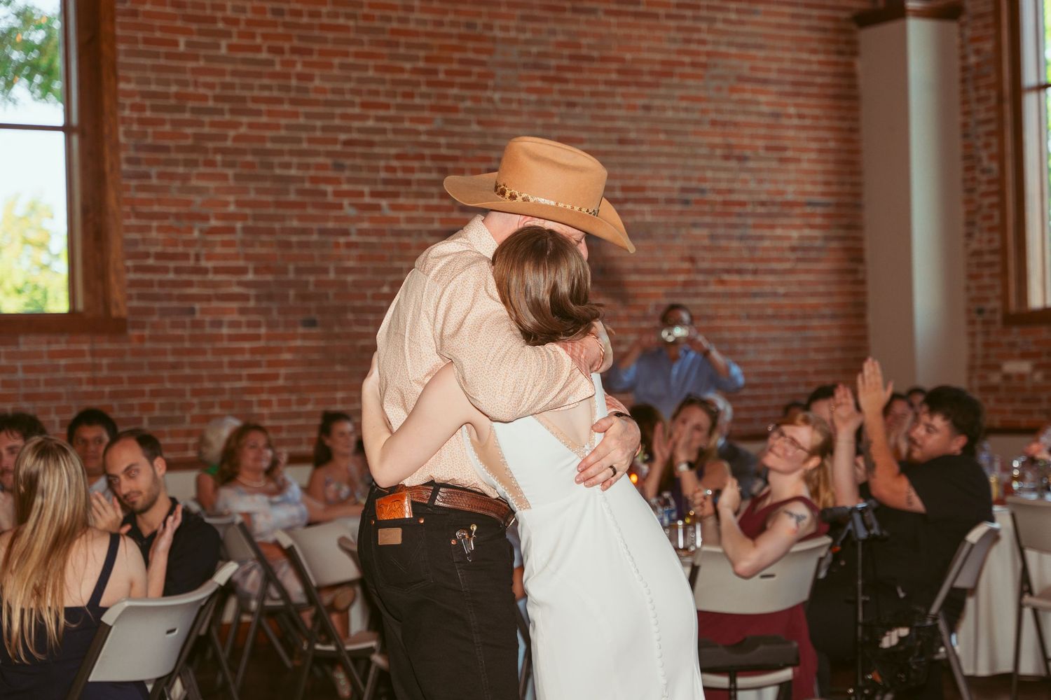 Couple shares a romantic dance at their wedding reception in a brick-walled venue.