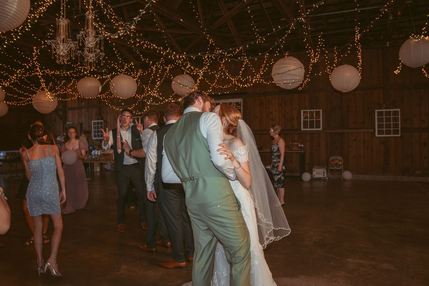 Wedding guests dancing in a rustic barn decorated with string lights and paper lanterns.