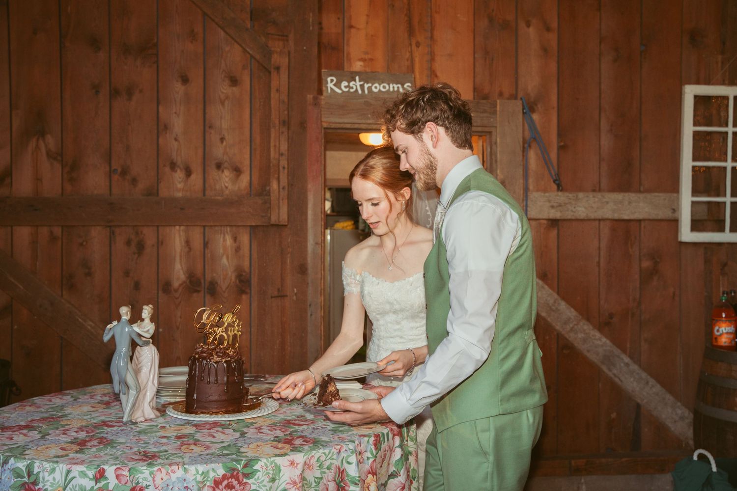 Couple laughs while sharing cake at their rustic barn wedding reception.