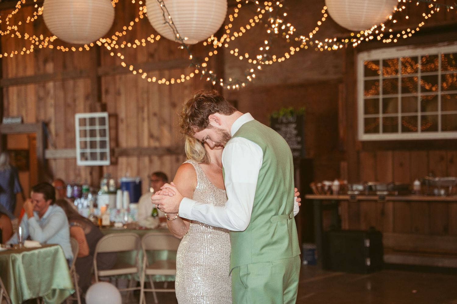 Intimate dance in beautifully lit barn venue with hanging lanterns and string lights.