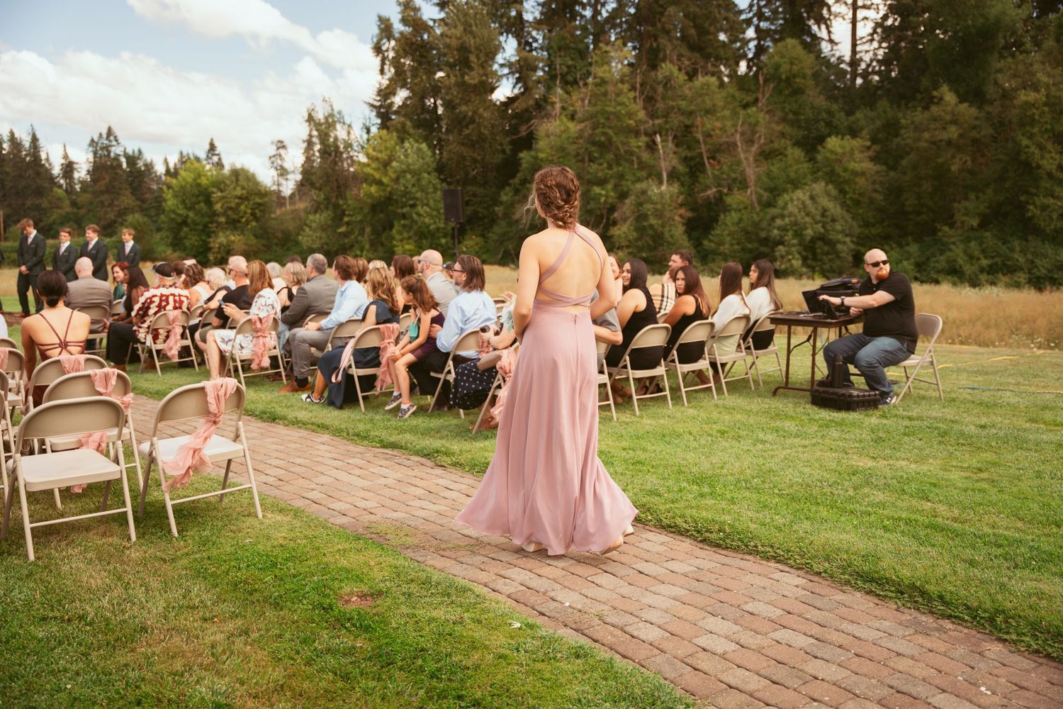 Outdoor wedding ceremony setup with rows of chairs on grass near a brick pathway.