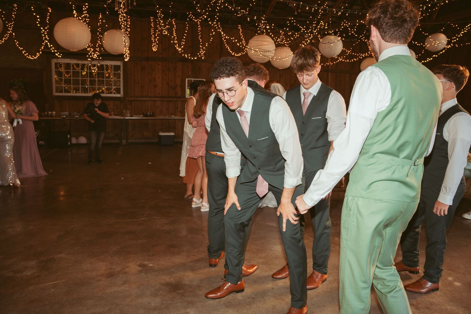 Group dance performance at a barn wedding with decorative lighting and paper lanterns.