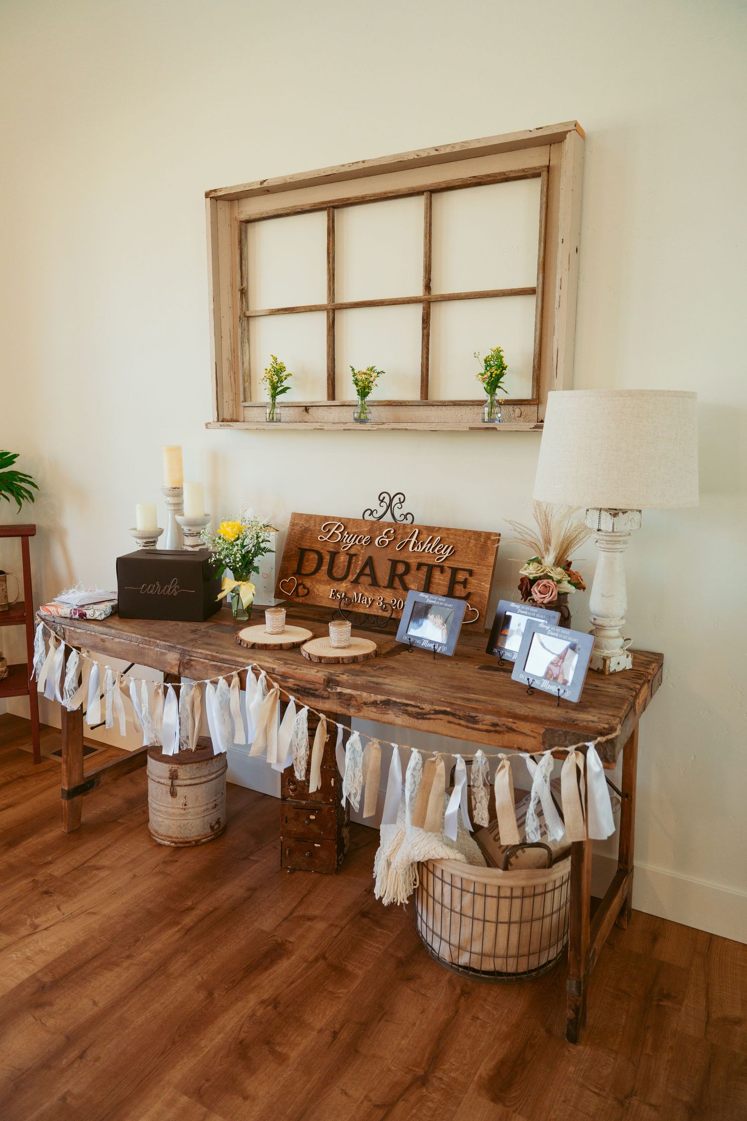 Rustic wedding reception setup with wooden tables, white fabric decor and vintage window frames.