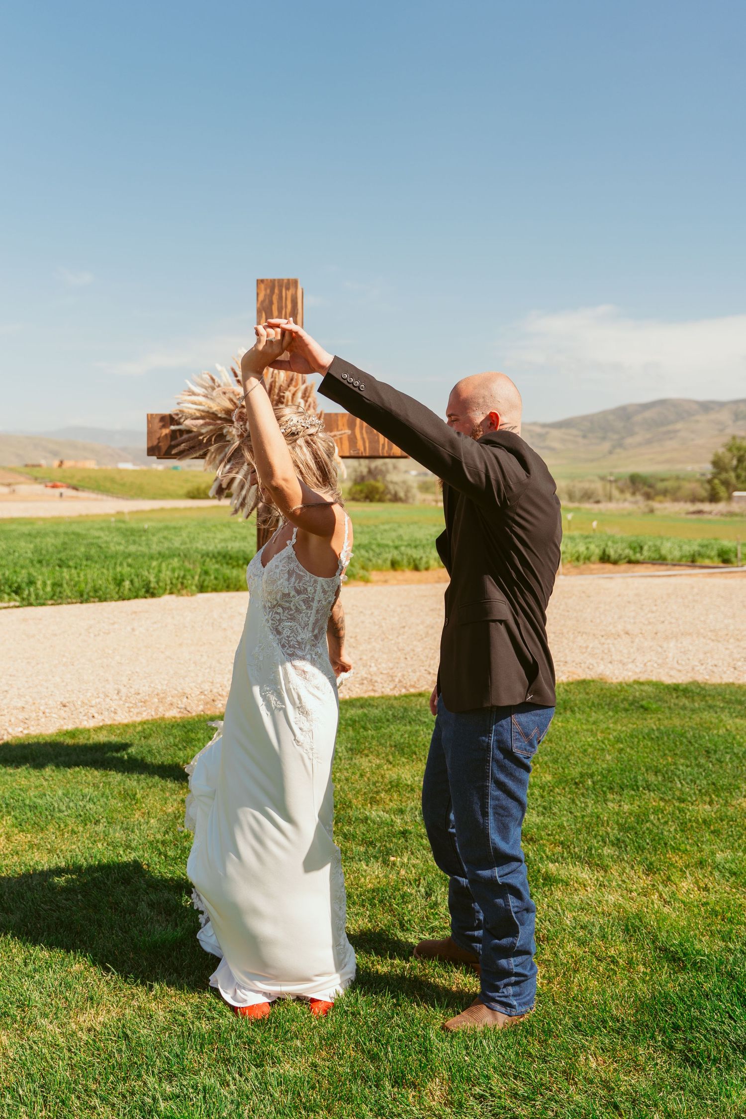 Couple performs playful dance moves on green lawn with mountains in background.