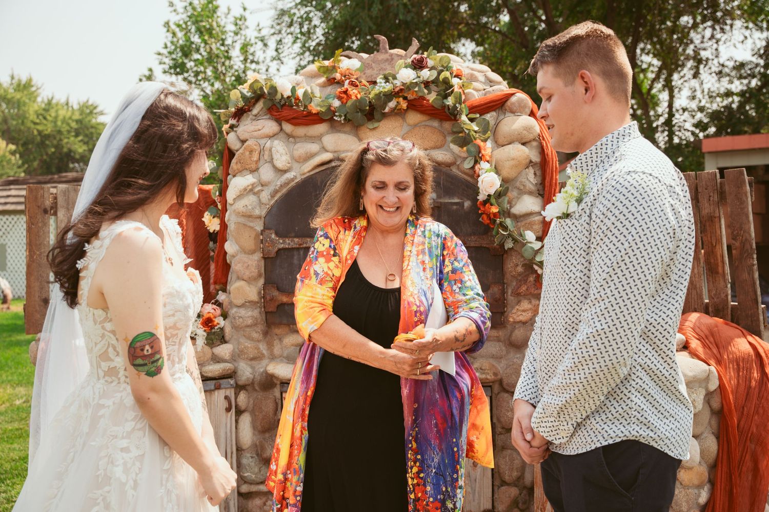 Wedding guests dance and celebrate under a rustic outdoor arch decorated with autumn florals and greenery.