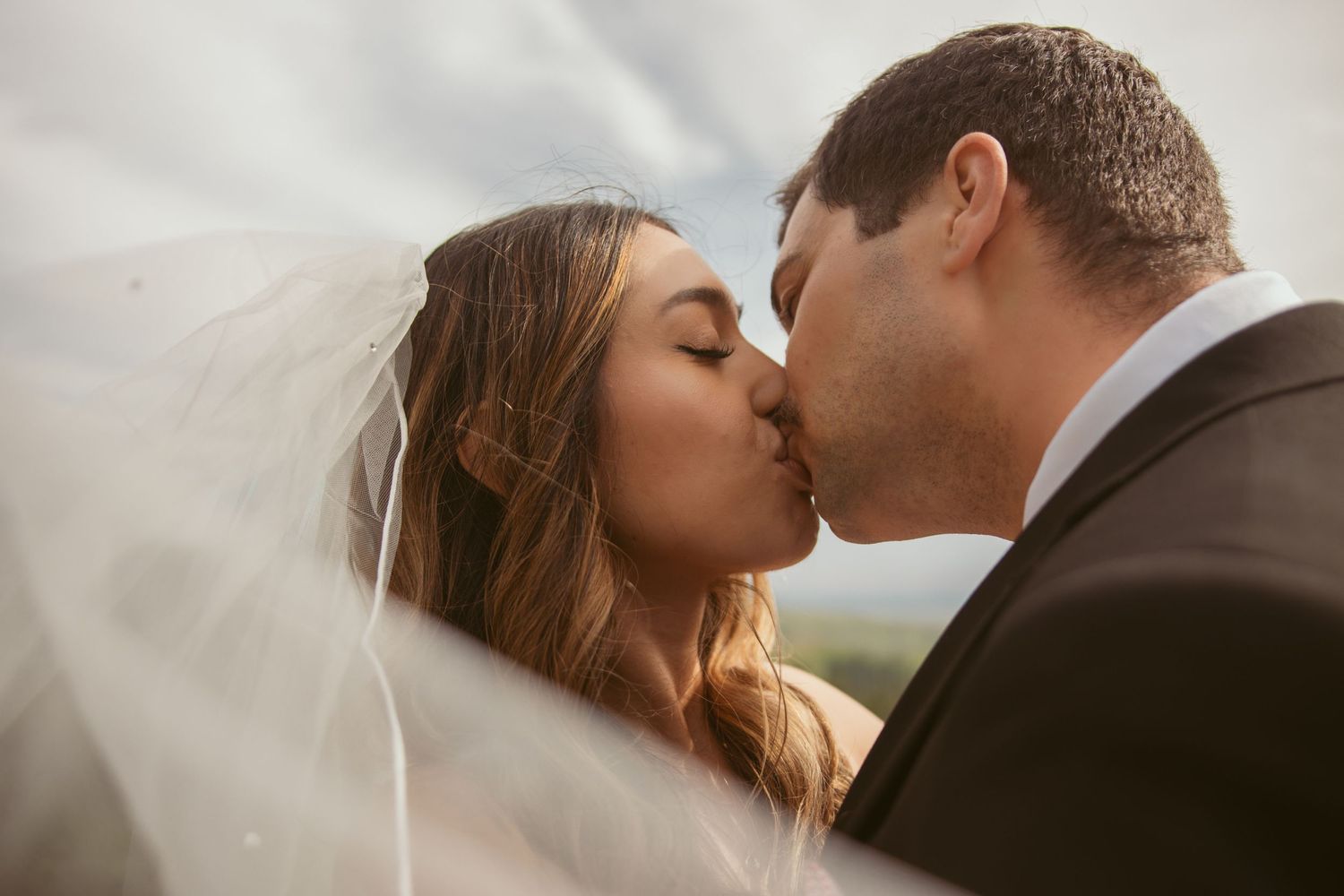 A romantic wedding kiss captured with a flowing veil in soft natural light.