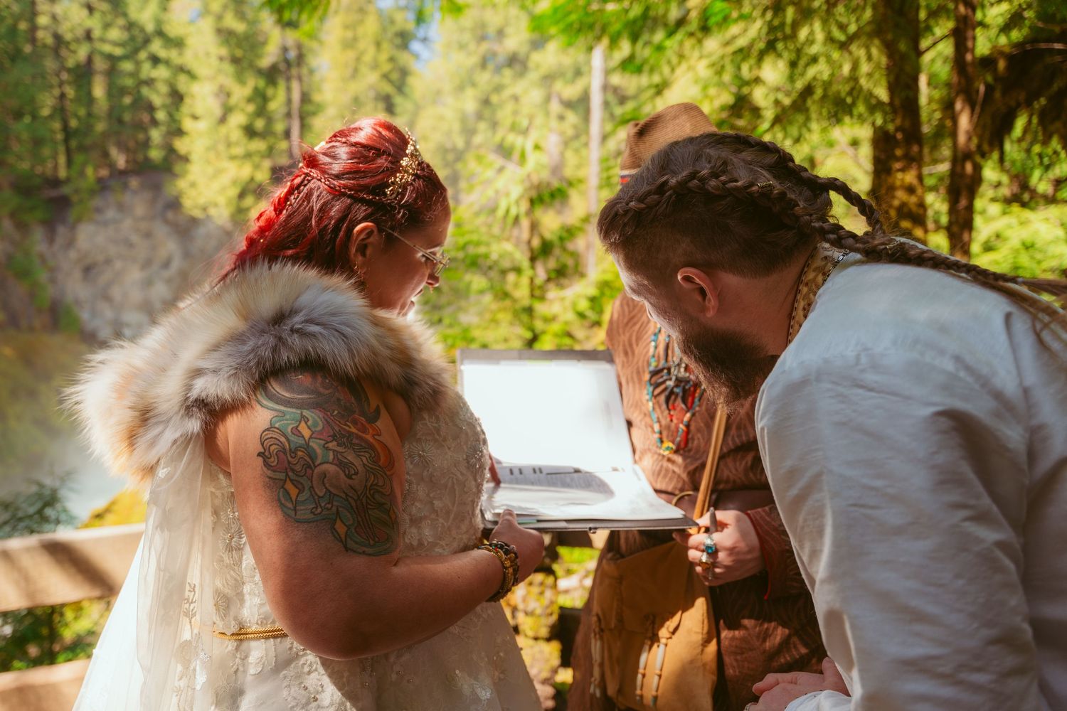 Couple in medieval-inspired wedding attire sharing a moment at a wooden table outdoors.