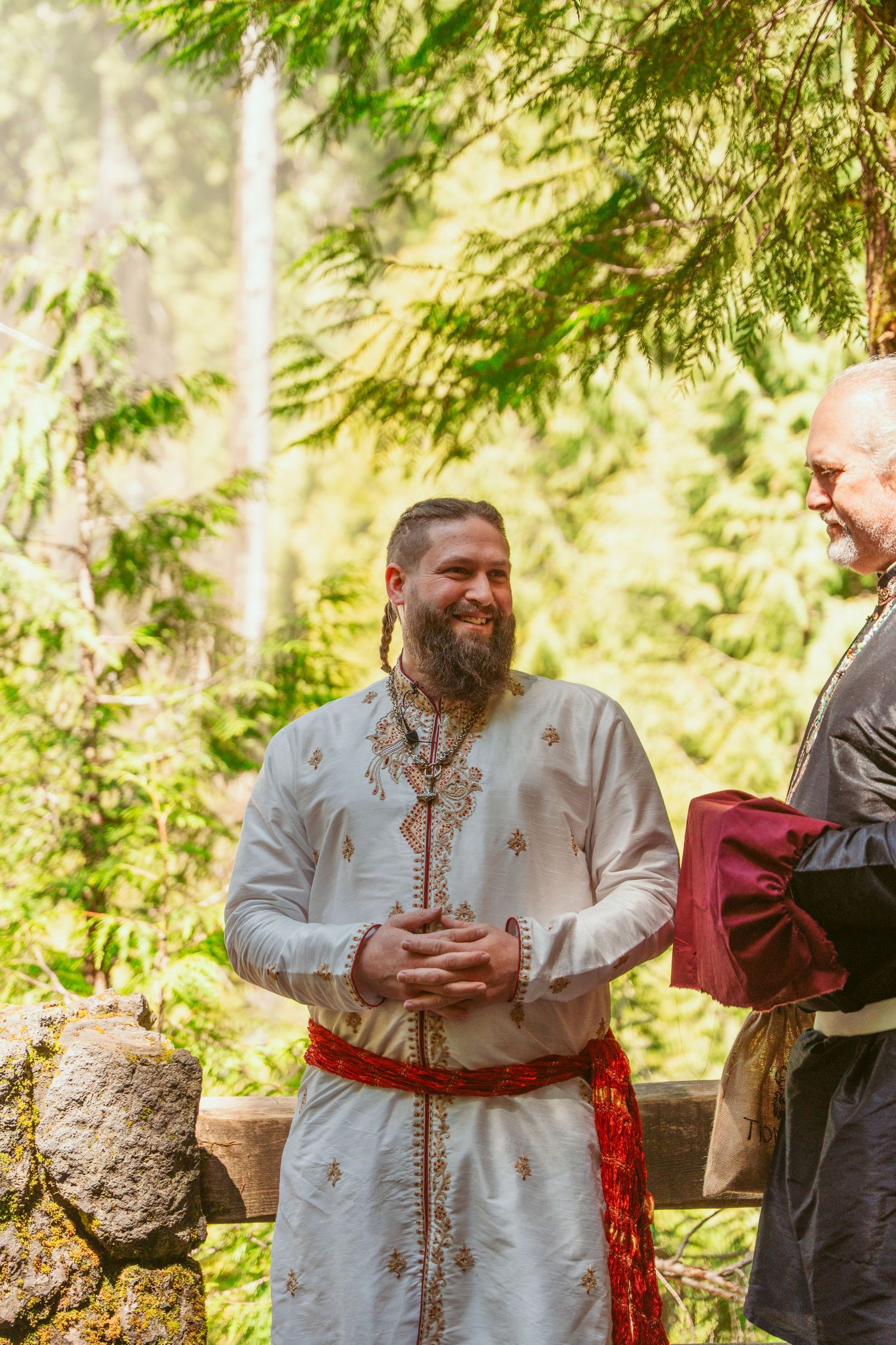 Traditional ceremony in forest setting with person wearing ornate white garments.
