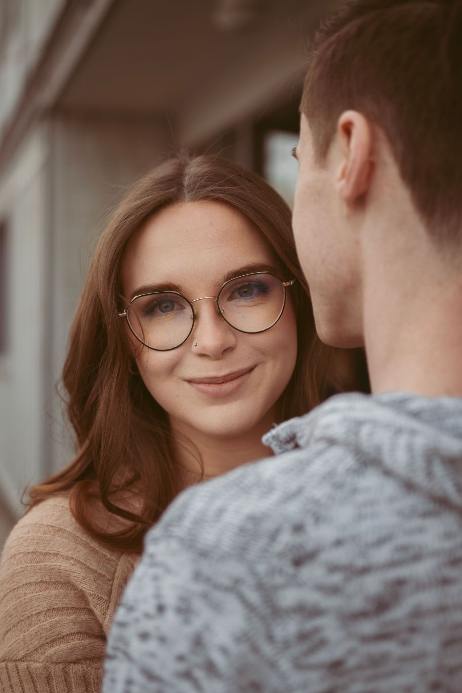 A close-up portrait of someone wearing round glasses and a beige sweater smiling warmly.