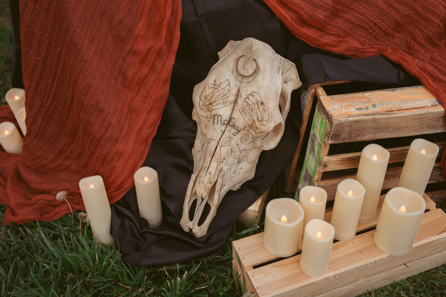 Decorative display featuring white candles, animal skulls, and rustic elements on a red cloth.