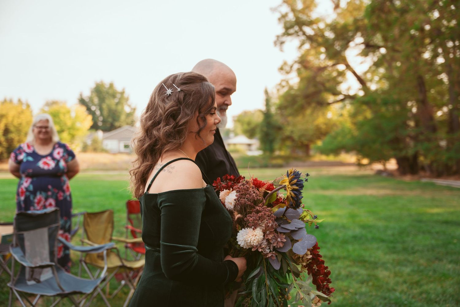 Two people interact outdoors on a grassy lawn with trees visible in the late afternoon sunlight.