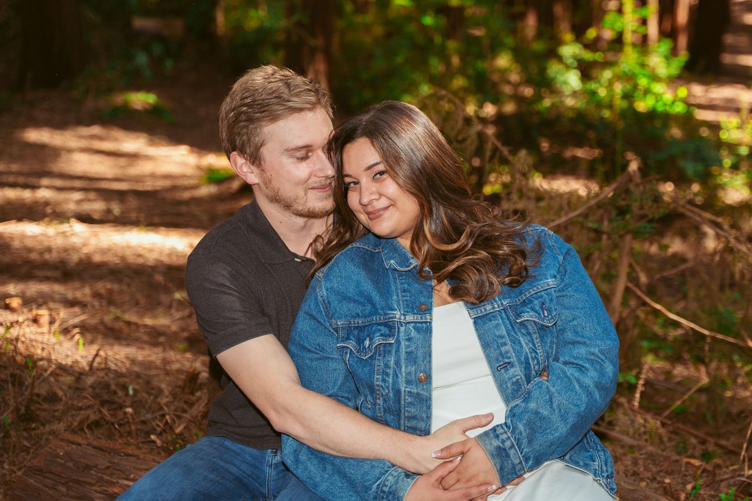 A couple enjoys an intimate moment together in a sunlit forest setting.