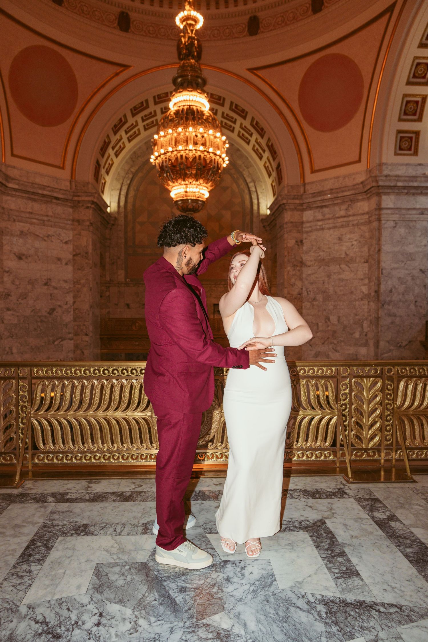 A romantic couple poses together in a grand marble hallway with ornate architectural details.