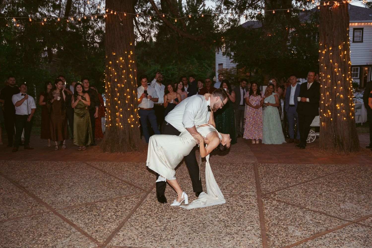Wedding reception dance floor filled with guests celebrating under outdoor string lighting.