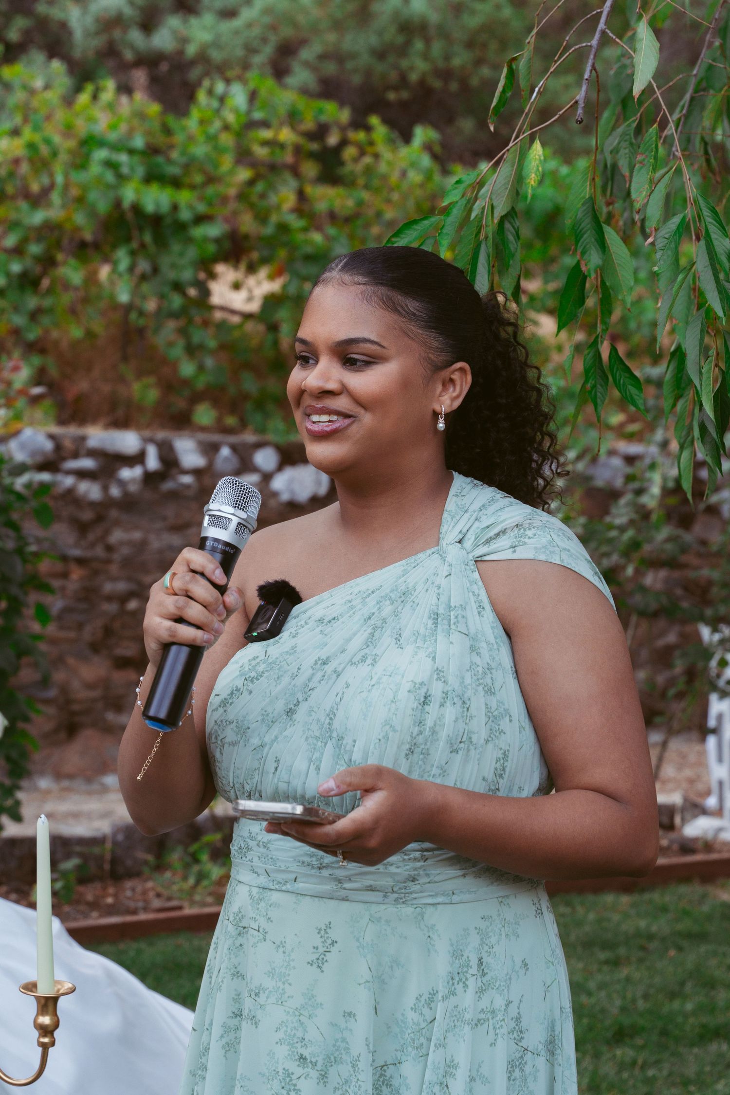 A person in a mint green dress delivers a speech while holding a microphone at an outdoor event.