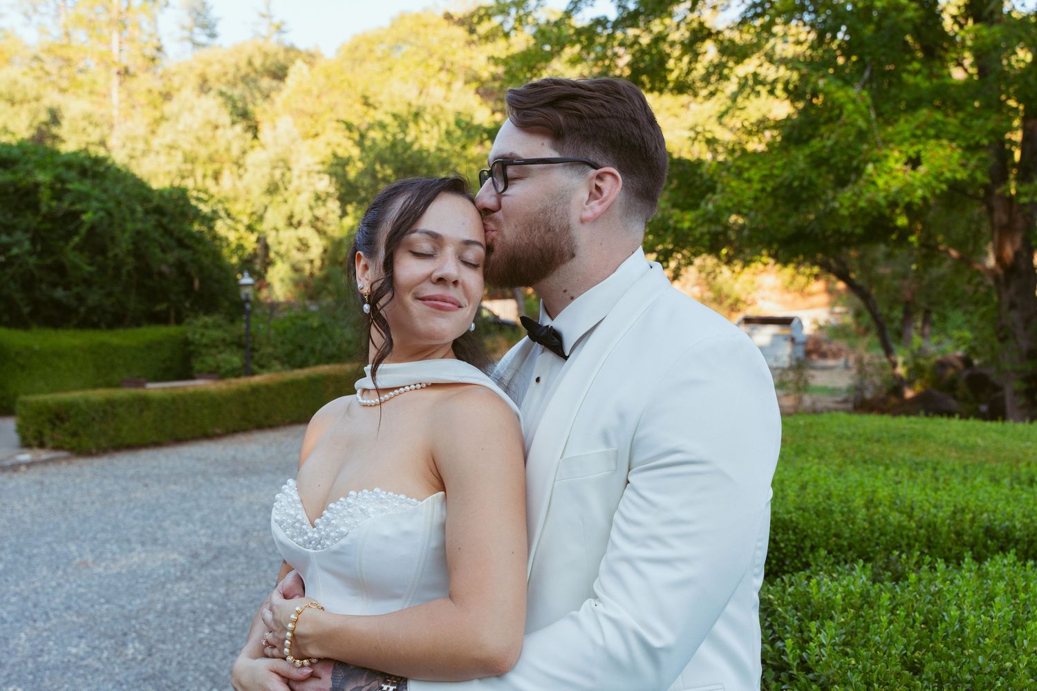 A couple shares a romantic moment in formal attire against a golden sunset backdrop.