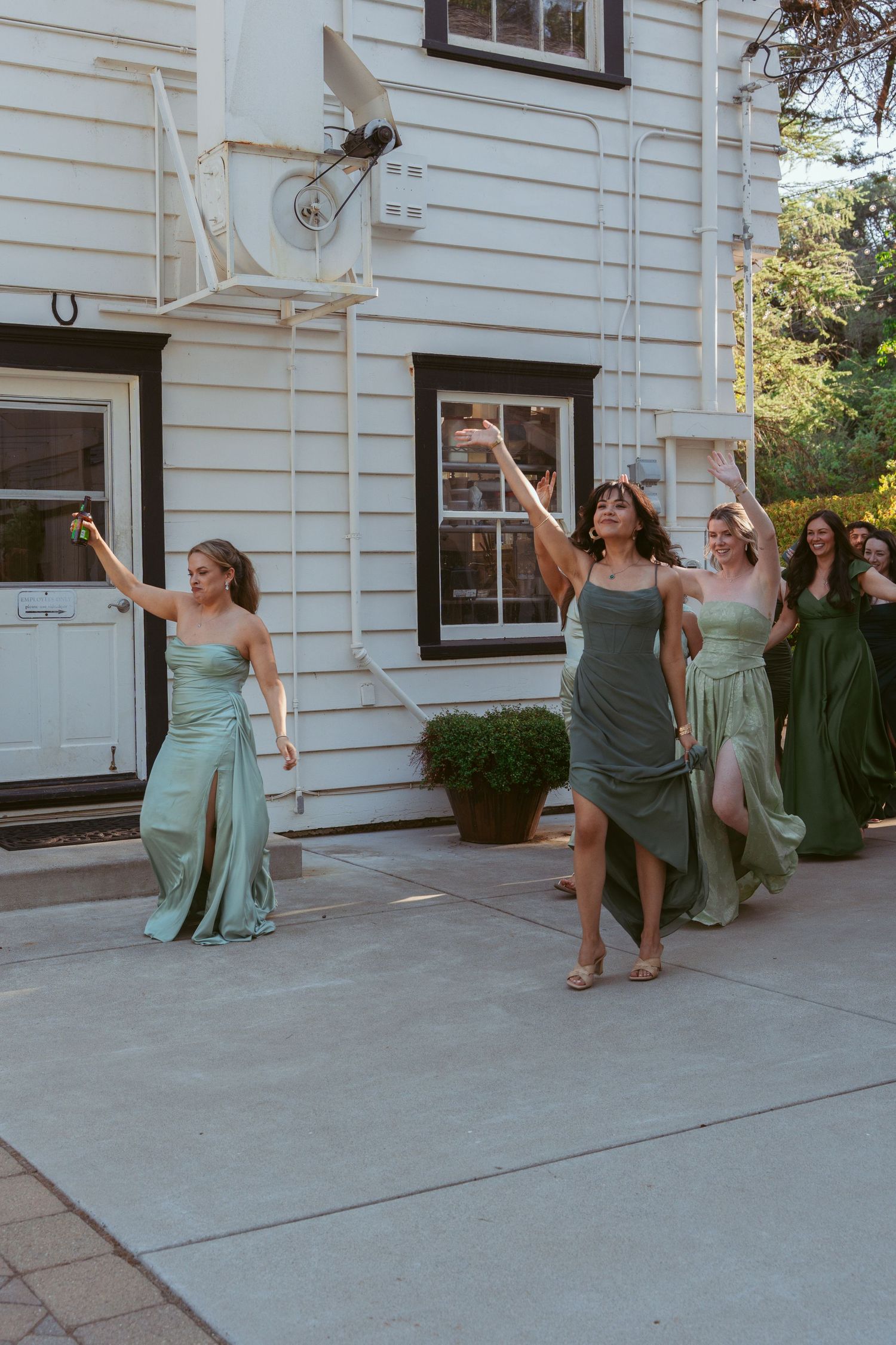 Wedding party members in mint green dresses posing playfully outside a white building.