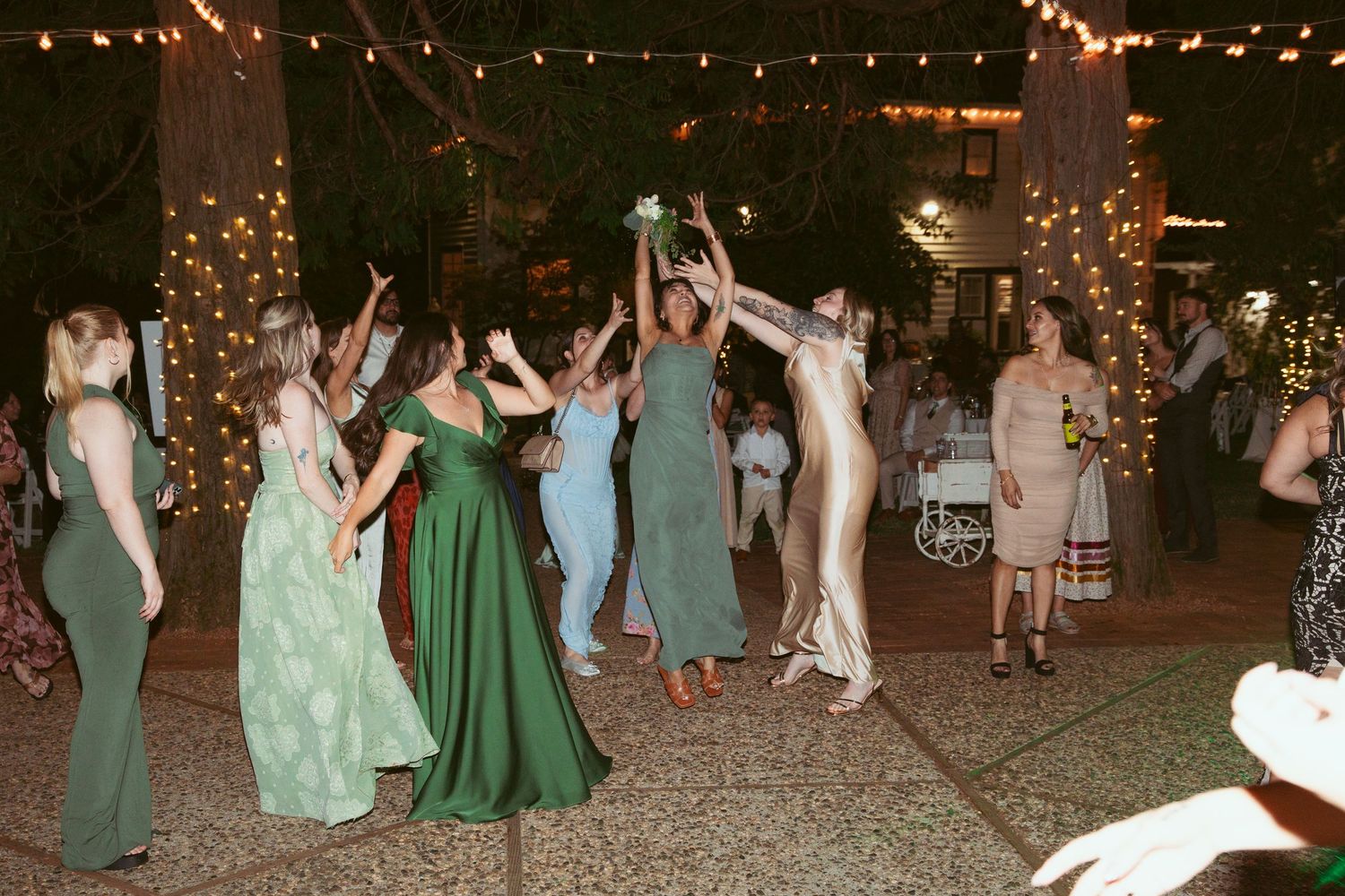 Wedding guests dancing under twinkling string lights at an outdoor evening celebration.