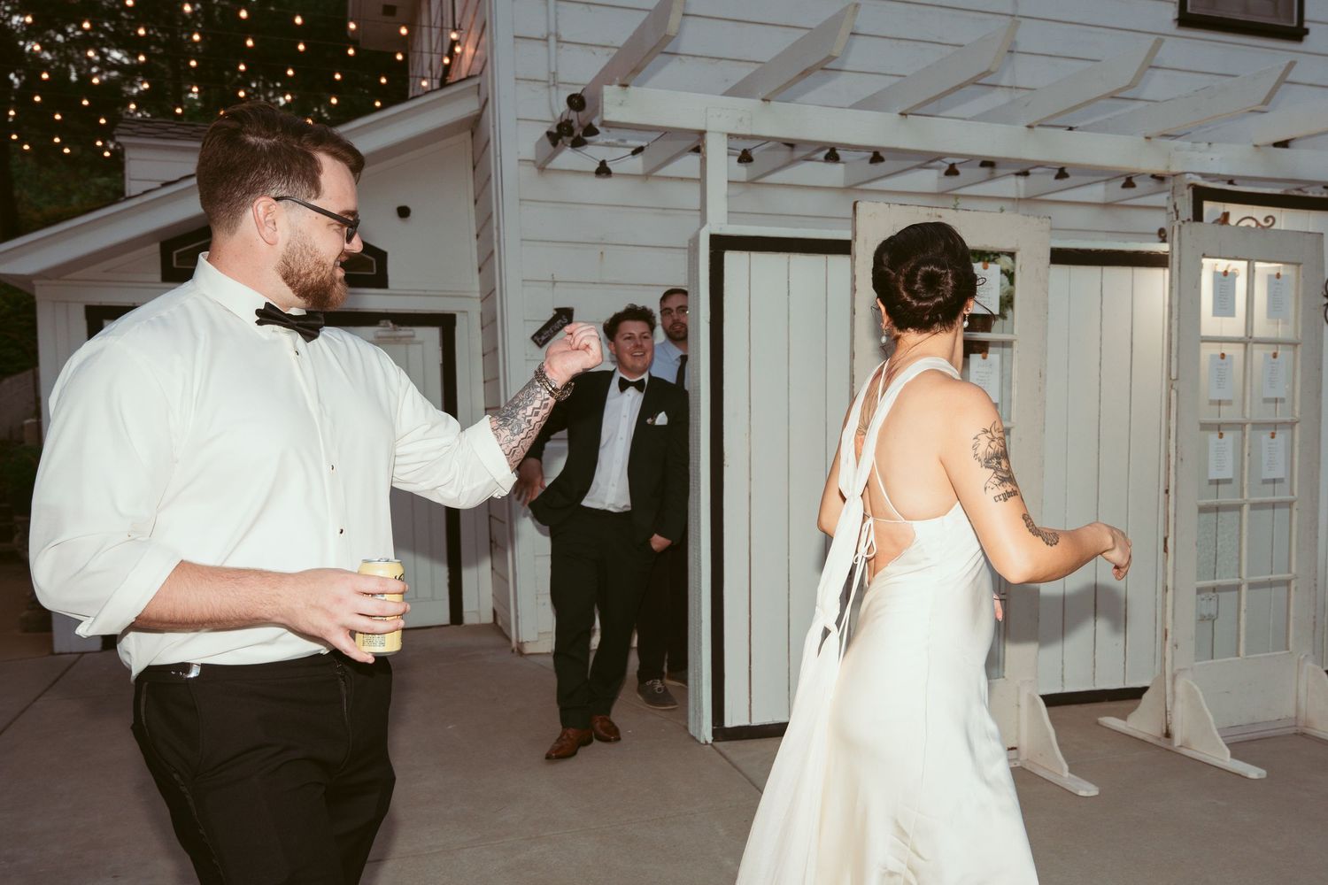 Wedding reception dance party inside a white-walled venue with string lights overhead.