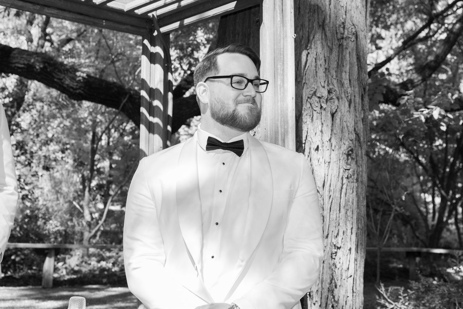 Black and white wedding photos displayed in a filmstrip style showing romantic moments under a rustic wooden pergola.