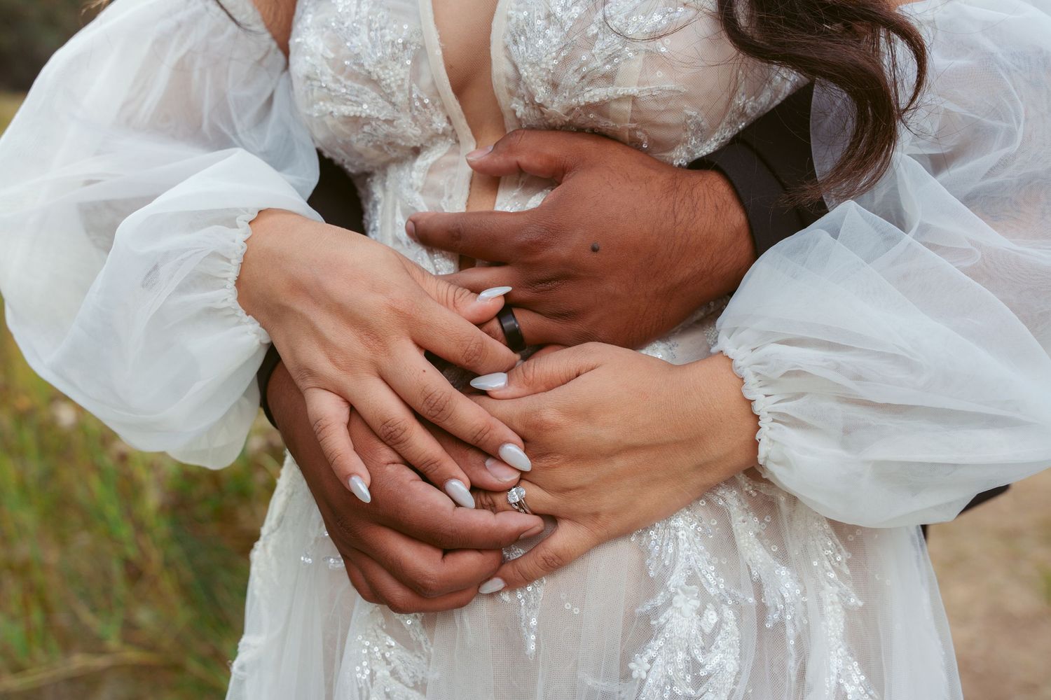 Close-up of hands with wedding rings against white lace dress fabric.