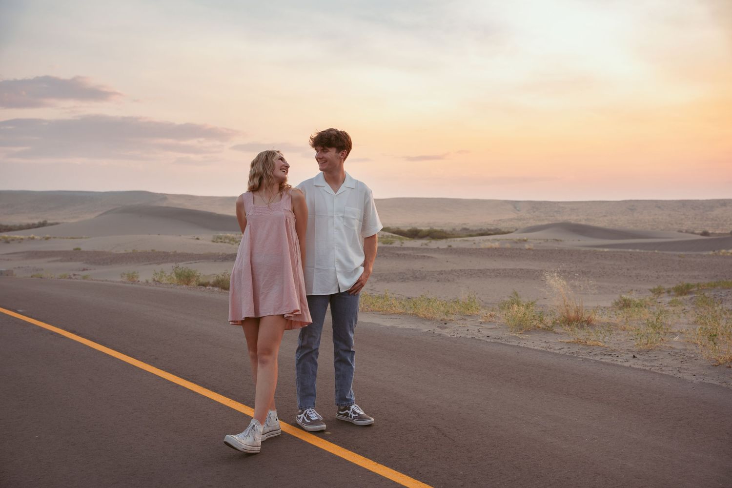 Desert landscape with couple standing on empty road at sunset.
