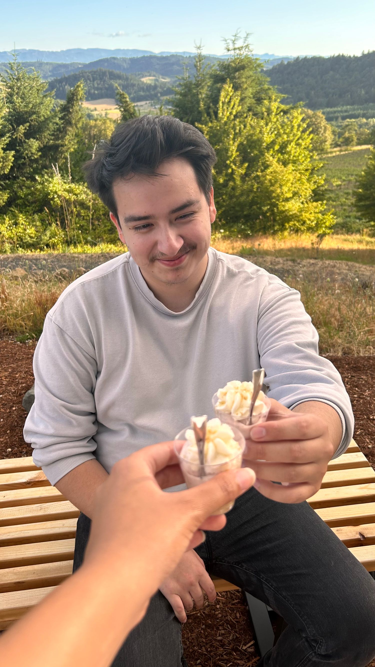 Someone examines a small object while sitting at an outdoor bench with mountains in the background.