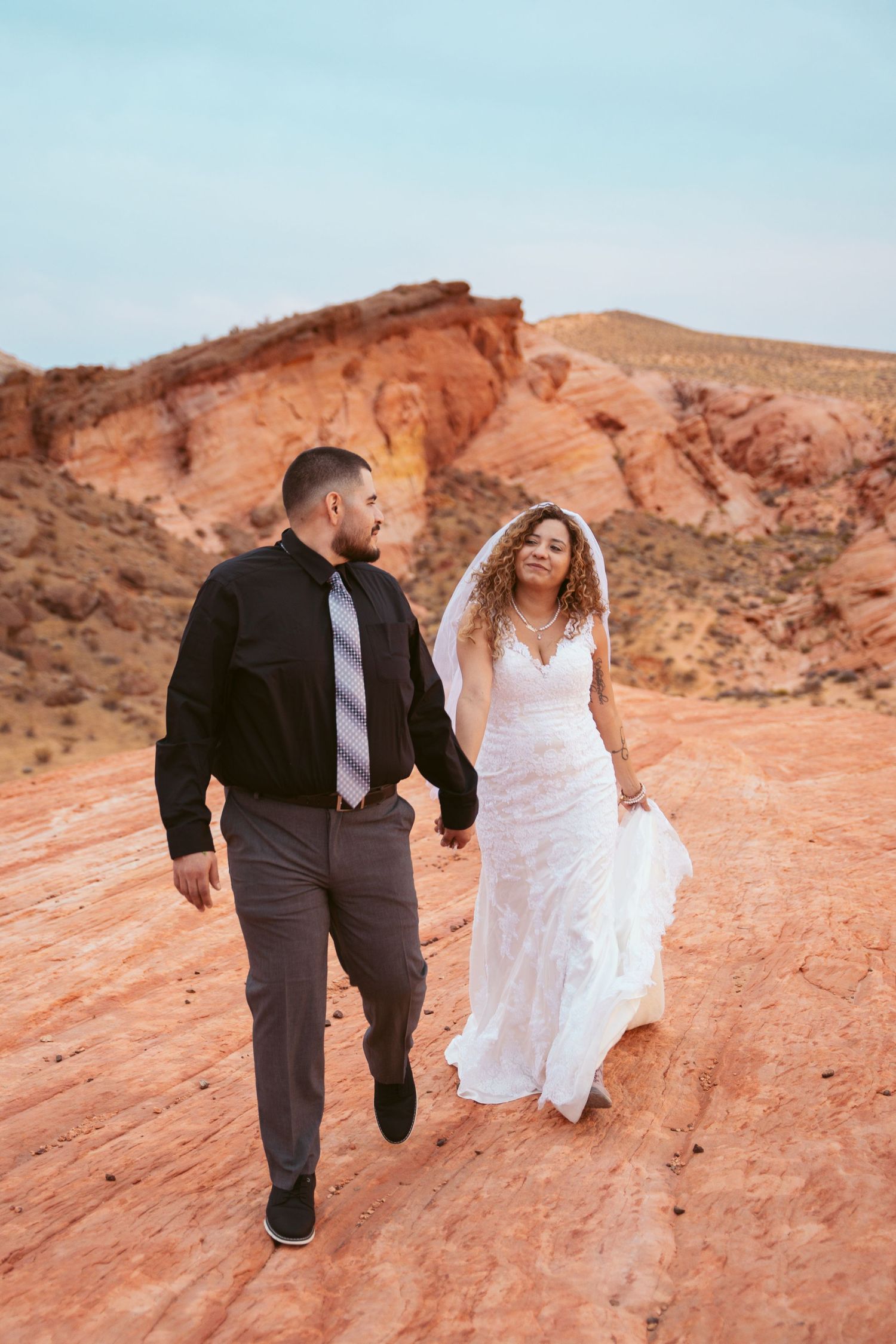 Playful wedding couple runs across red desert rocks during photo session.