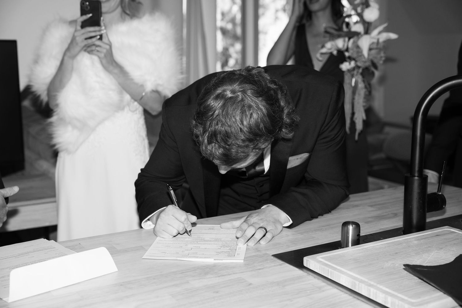 Person signing important documents at a kitchen counter in formal attire.
